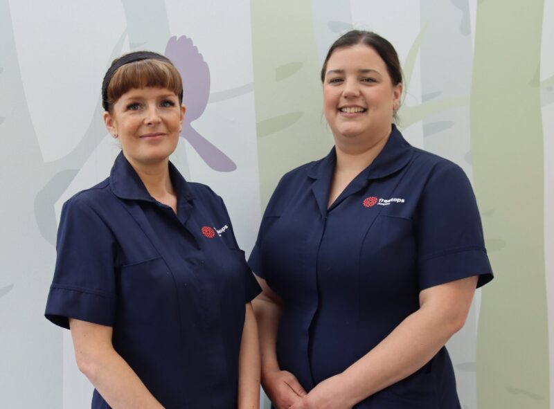 Two white hospice nurses in dark blue uniform standing together