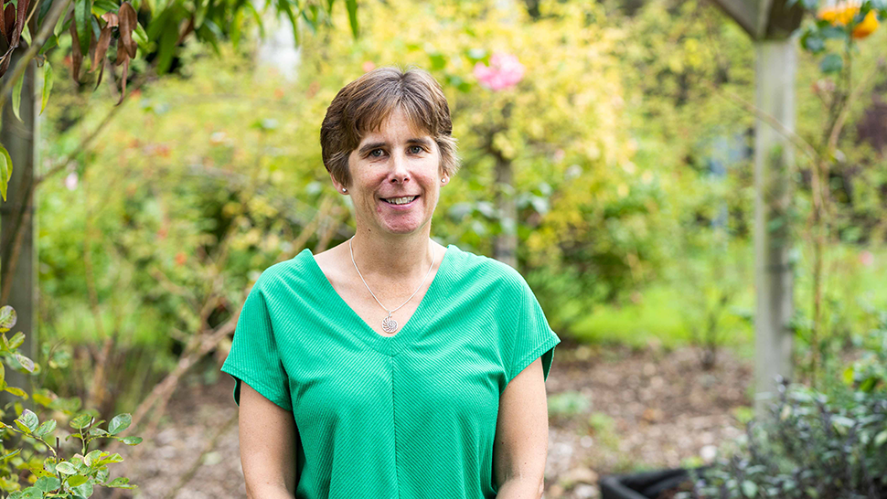 A woman with broiwn hair smiling in a green t-shirt standing in the Treetops grounds