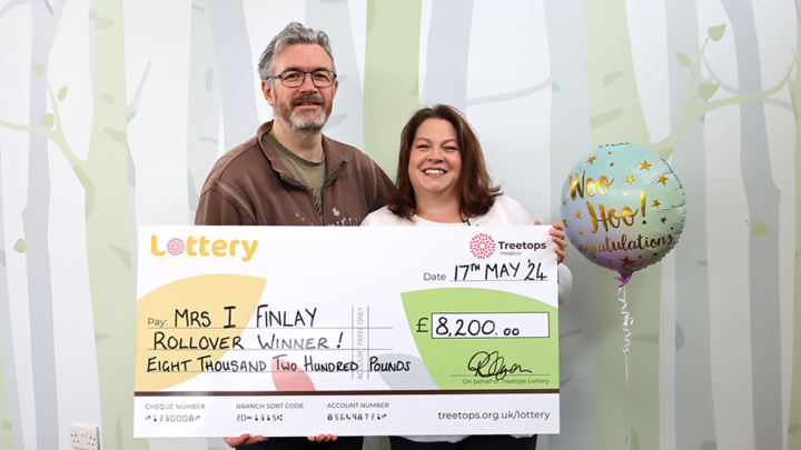 Smiling couple holding a giant Treetops Lottery cheque for the rollover prize of £8,200