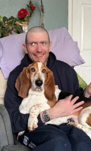 Man sitting in bed with basset hound dog on his lap smiling