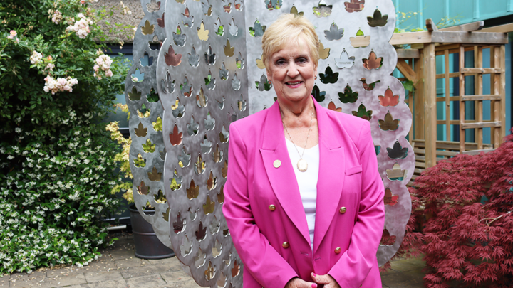 Woman in pink suit smiling in front of Treetops memory Tree