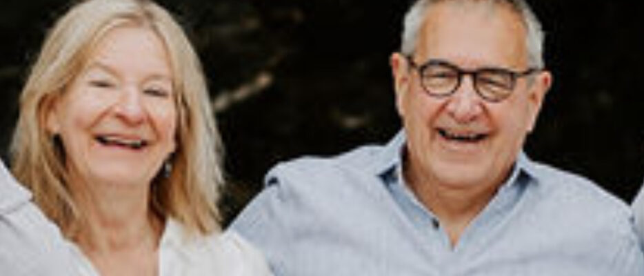 Man and woman smiling. Woman has long blonde hair and man has short grey hair and glasses.