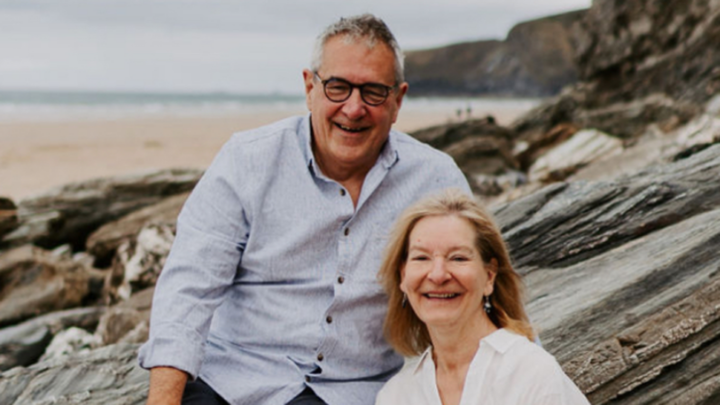 Couple smiling sitting on rocks at the seaside with the beach and sea in the background