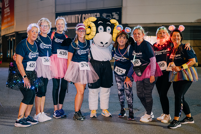 Group of people cheering in Moonlight Walk t-shirts next to Derby County Football Club mascot Rammie. Photo credit: JAKT Photography