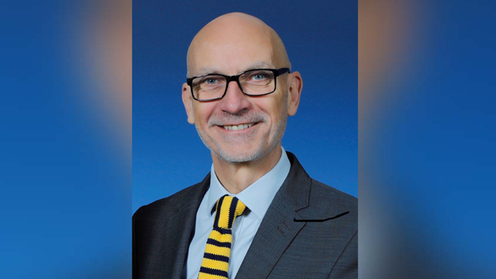 A portrait photo of a man wearing a suit smiling at the camera wearing glasses