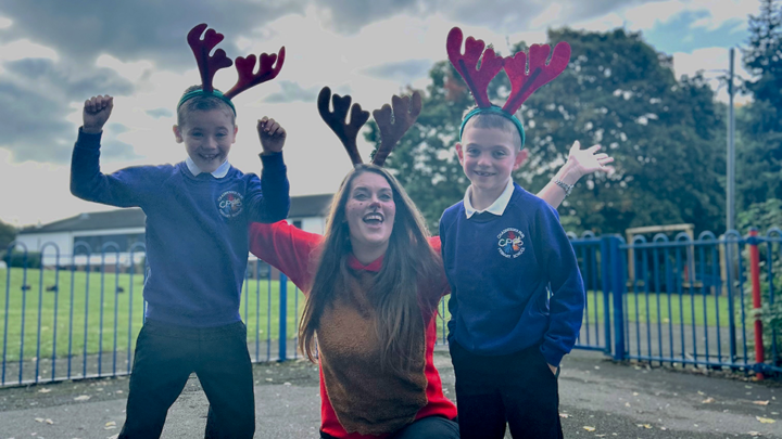 Woman dressed as reindeer sitting between two primary age children all cheering