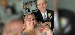 Married couple in bridal outfits smiling and holding glasses of fizz