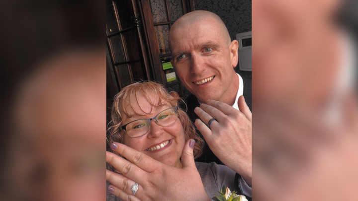 Young couple dressed in bridal outfits holding their new wedding rings up to the camera and smiling