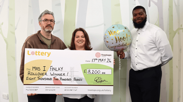 Smiling couple holding a giant Treetops Lottery cheque for the rollover prize of £8,200