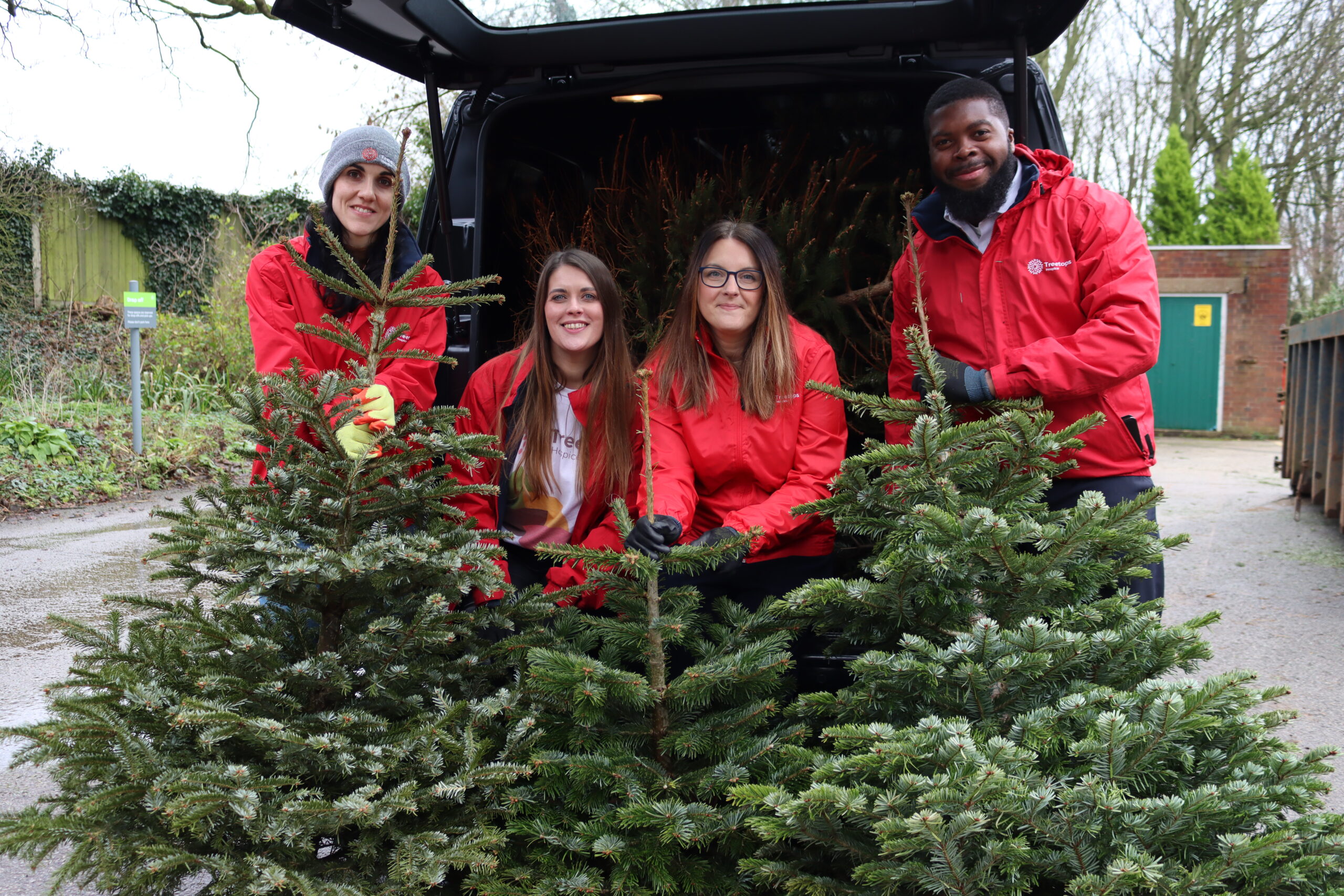 4 people wearing red standing with christmas trees