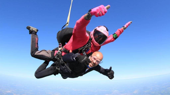 A tandem skydive with two men free falling and smiling at the camera