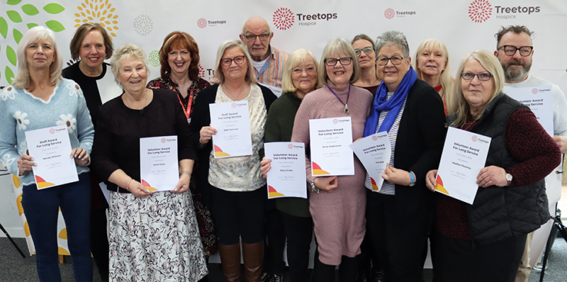 Group of smiling men and women holding long service awards at Treetops Hospice