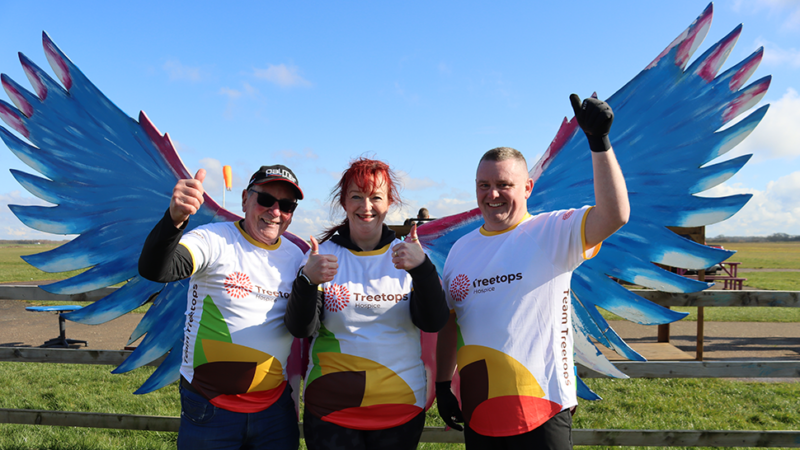 Three skydivers in Treetops t-shirts standing in front of a pair of giant wings